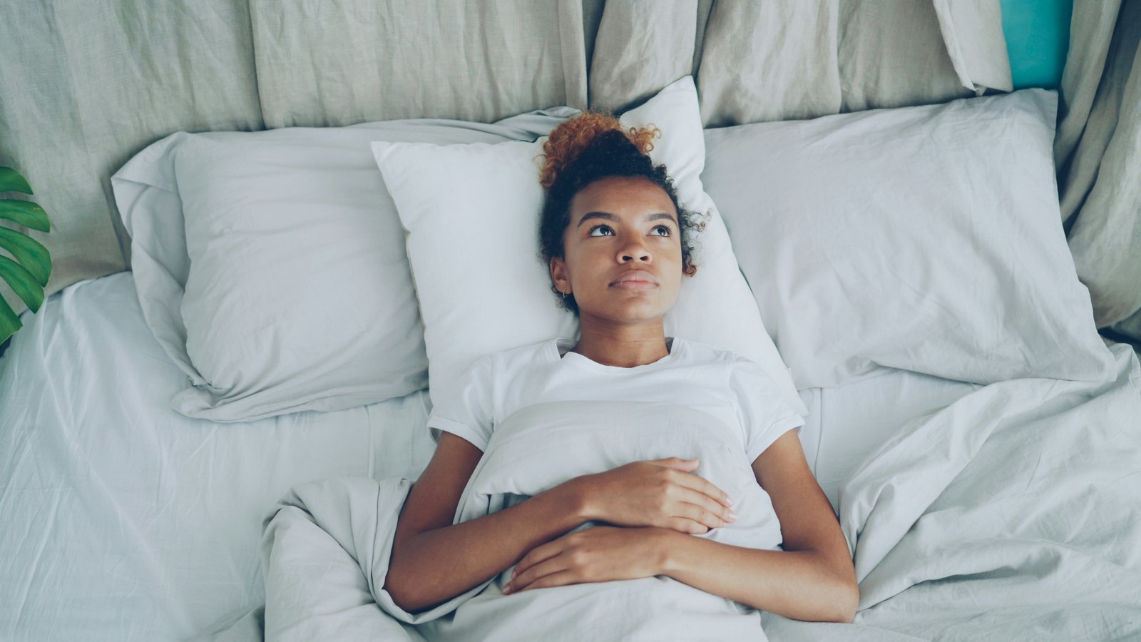 A young woman lying in bed with her hands resting on her lower abdomen